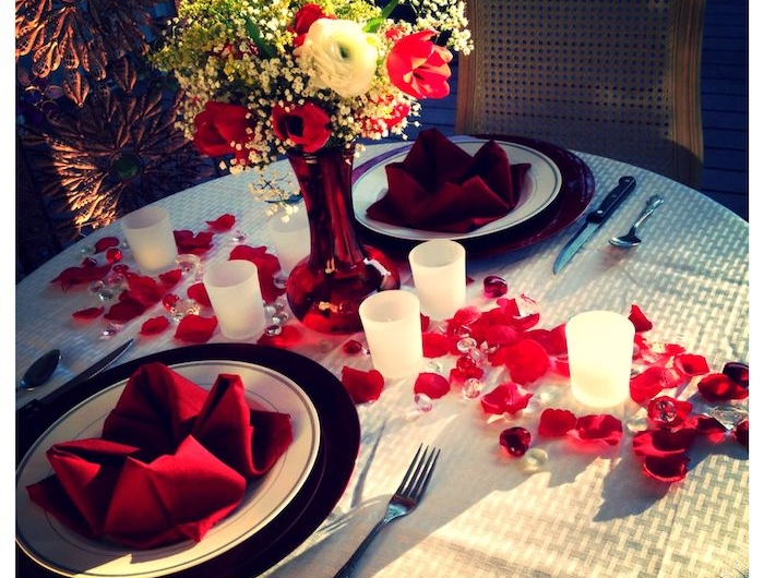 idée repas amoureux avec deux serviettes rouges dans des assietes chemin de table en petales et chandelles