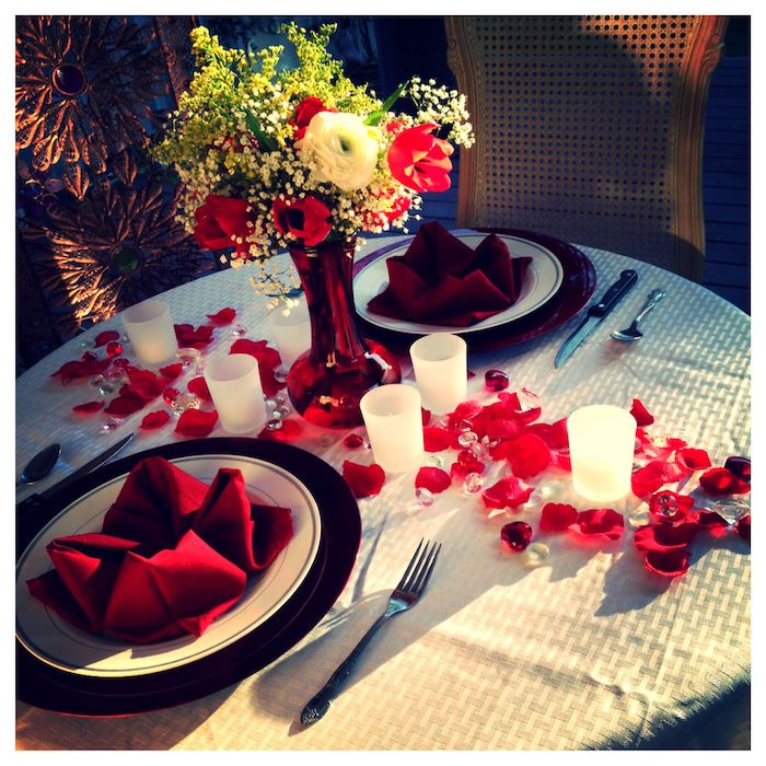 idée repas amoureux avec deux serviettes rouges dans des assietes chemin de table en petales et chandelles