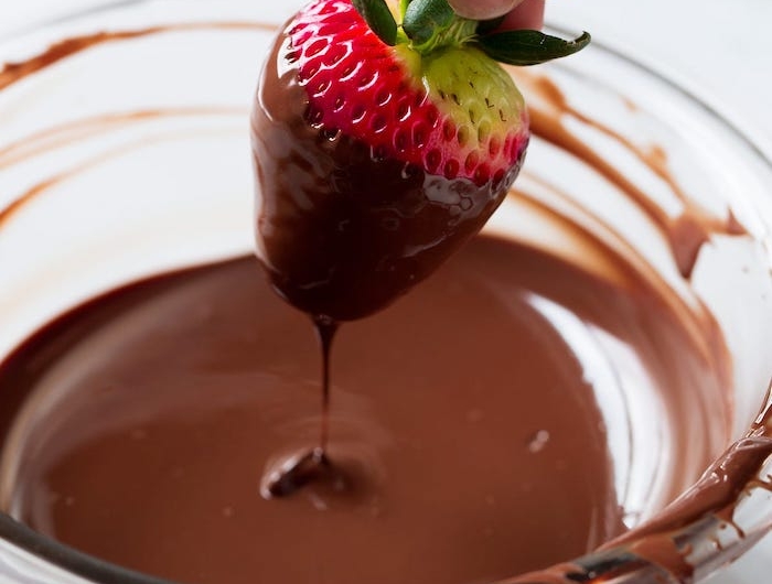idée repas en amoureux un main qui trempe une fraise dans du chocolat fondu