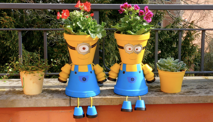 personnage en pot de fleur des miniions décoratives assises au bord d un jardin a coté des deux fleurs.jpg
