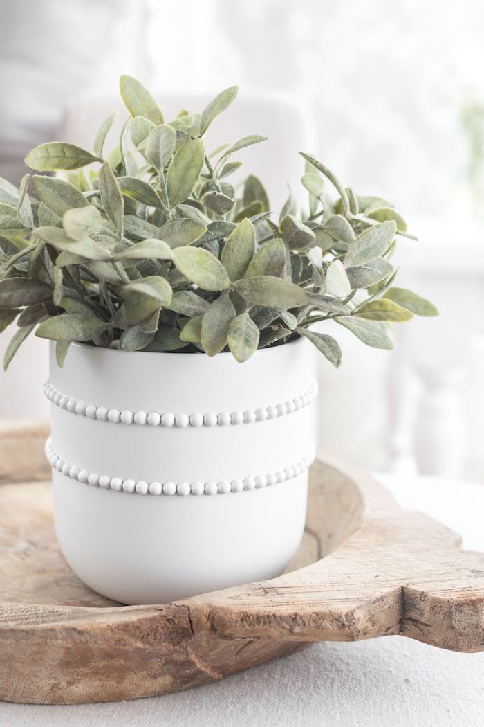 pot de fleur original en)blanche avec deux rangés des perles fausses posé sur un plateau rustique en bois