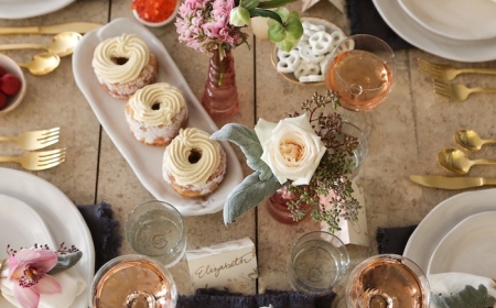 table saint valentin avec des patisseries et des verres remplies de vin rose et couvert dorees