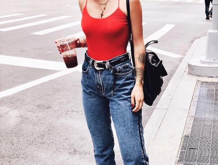 tenue avec jean mom un top décolté rouge et des basketes vans une femme)dans la rue qui boit de coca