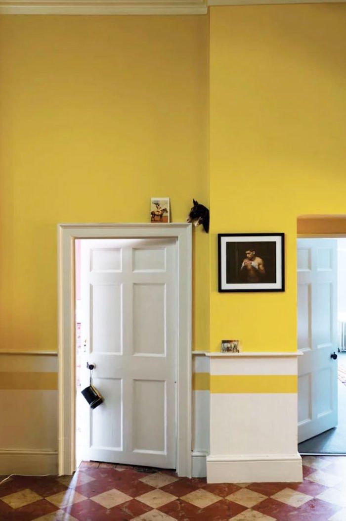 un couloiur peint en deux couleurs blanc et jaune lumineux avec des carreaux bruns au sol t une porte en bois