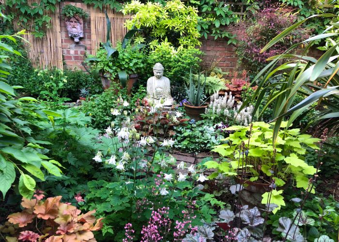 aménagement jardin zen avec pleine de végétation florissante pots de plantes mur de briques statuette bouddha