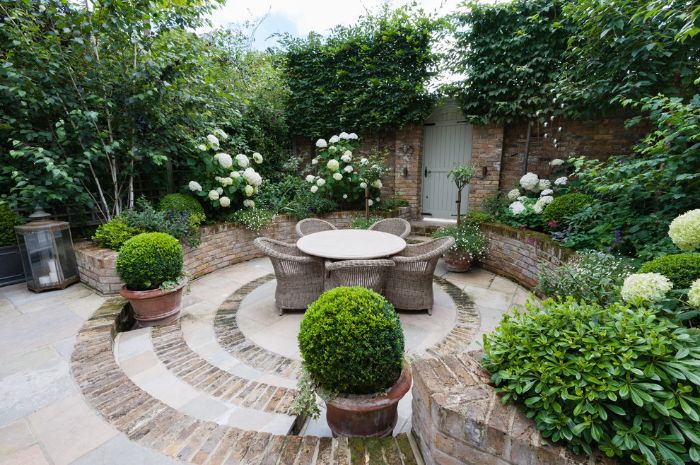 aménager sa terrasse extérieure en dalles et pierre salon de jardin rotin et table ronde vegetation tout autour plantes vertes et buis