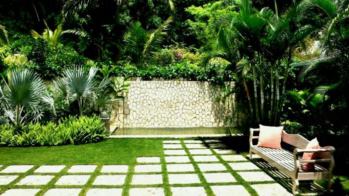 banc en bois dalles de beton sur gazon palmiers mur de pierre arbustes idee amenagement jardin