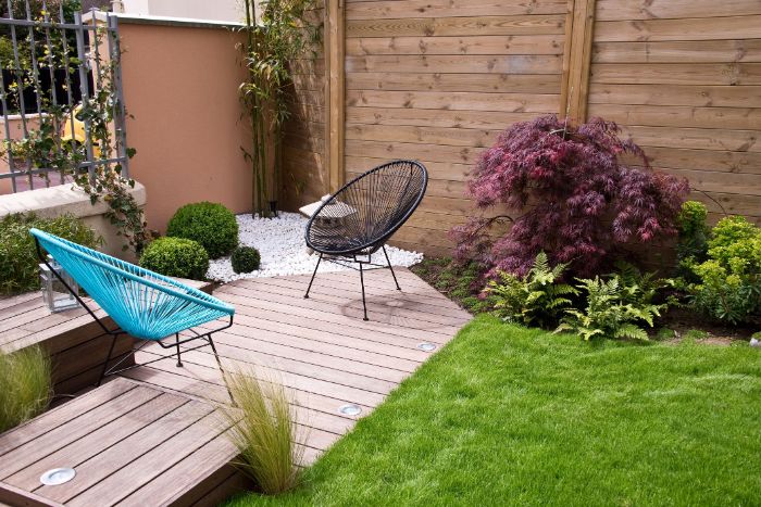 chaises en metal design sur une terrasse en bois dans un coin de jardin habiléde gazon et quelques plantes amenagement exterieur exemple