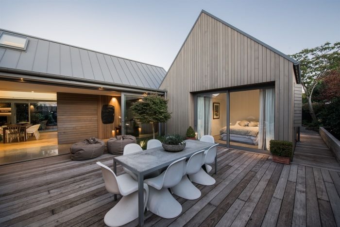 chambre ouverte sur terrasse en bois avec des chaises design blanches et plantes vertes en pot exterieur maison