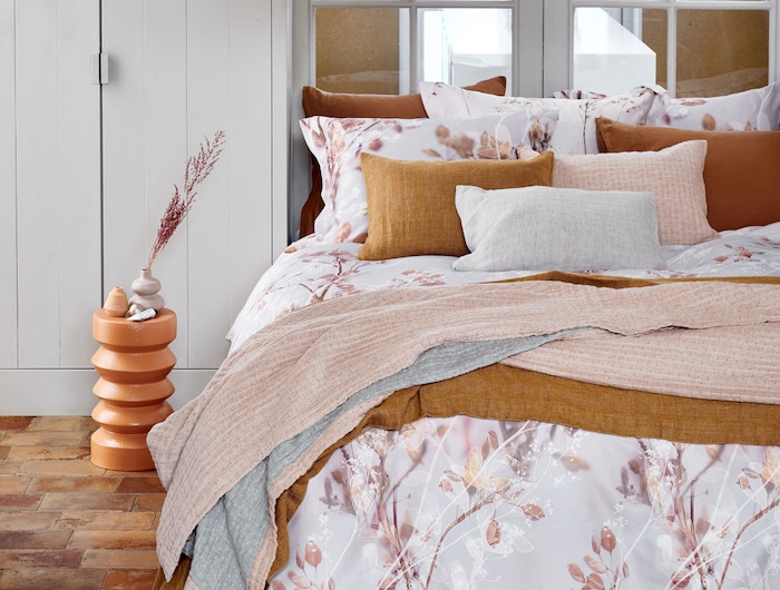 chambre rose et blanc avec de parquqet au sol et cousins en couleur orange sur le lit couvert d une couette a fleurs