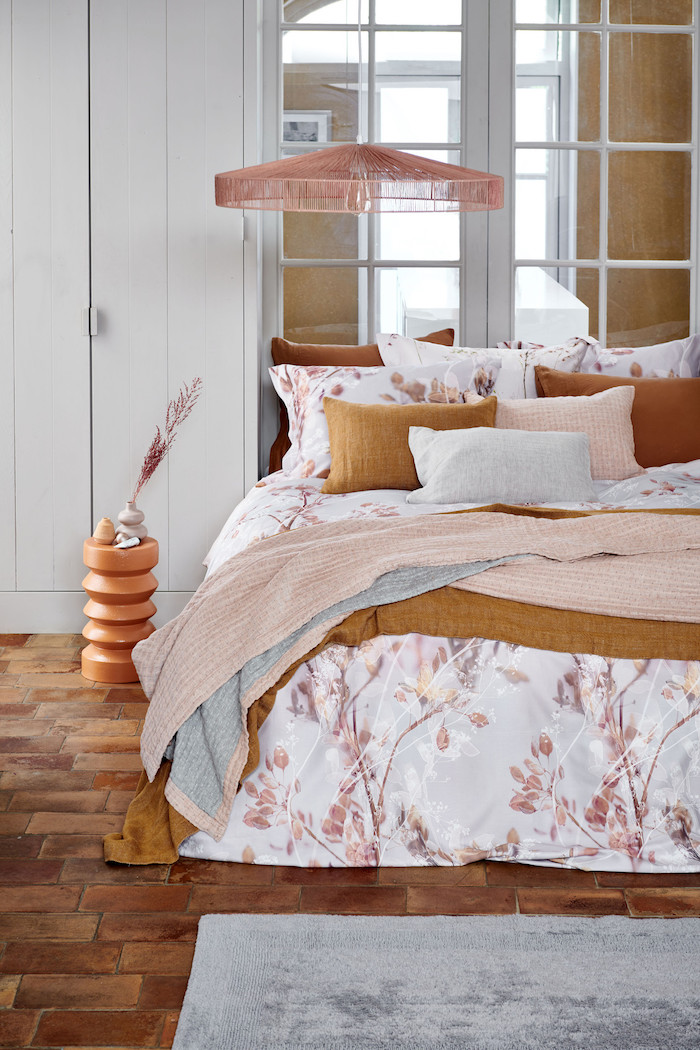 chambre rose et blanc avec de parquqet au sol et cousins en couleur orange sur le lit couvert d une couette a fleurs
