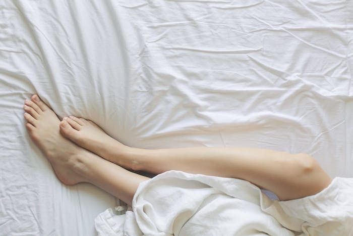 deux jambes feminines dans un lit avec des drapaeux blancs