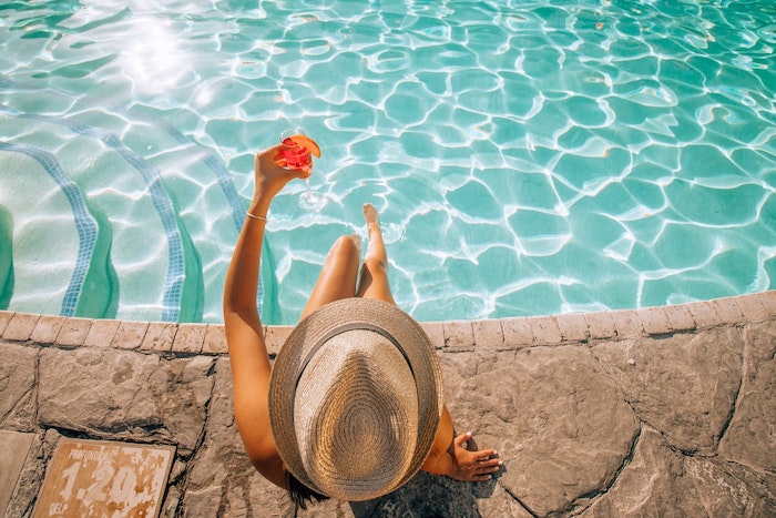 femme au bord de la piscine avec un coctail dans la main eau azure