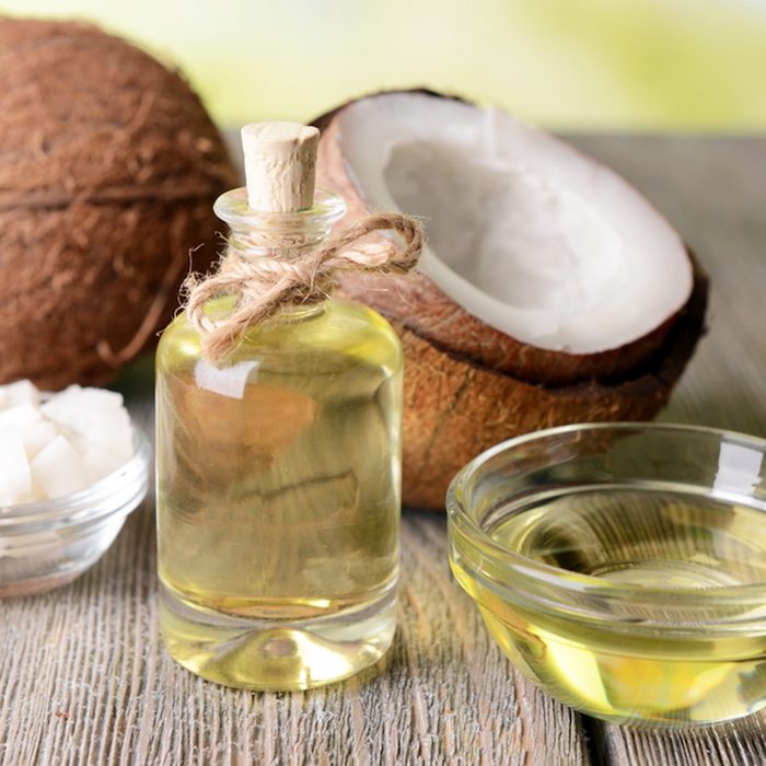 huile cheveux secs huile de coco dans une bouteille a coté d un noix de coco cassé