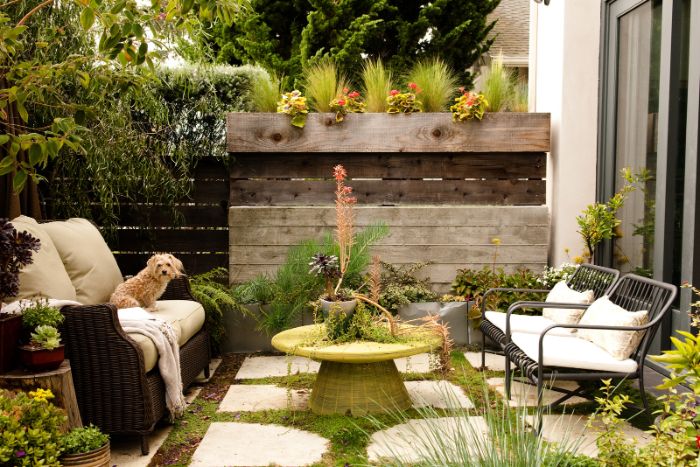 idee amenagement jardin avec chaises metaliques canapé en résine tressée mur palissade bois dalles de pierre sur gazon multitude de plantes