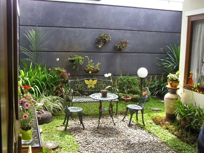 mur de cloture de beton gravier table et chaises metalliques gazon vert arbustes et plantes