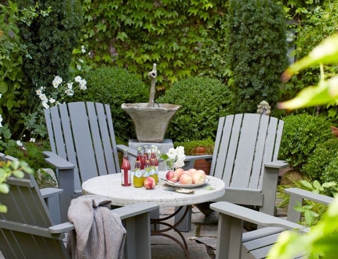 mur de jardin exterieure habillée de lierre avec table et chaises de bois grises et des dalles de béton végétation verte