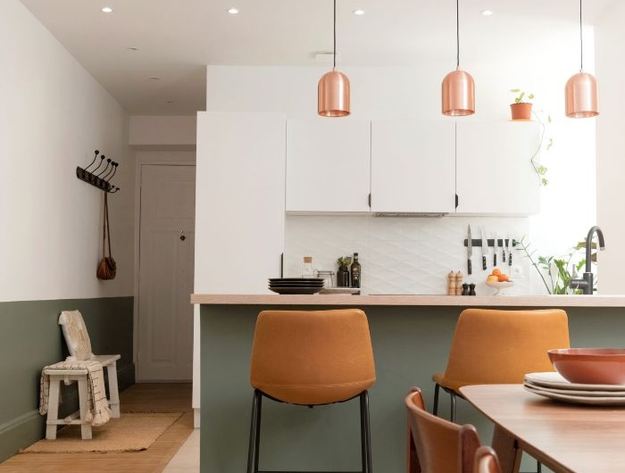 pan de mur et ilot central gris cuisine blanche avec des suspensions cuivre et salle à manger bois