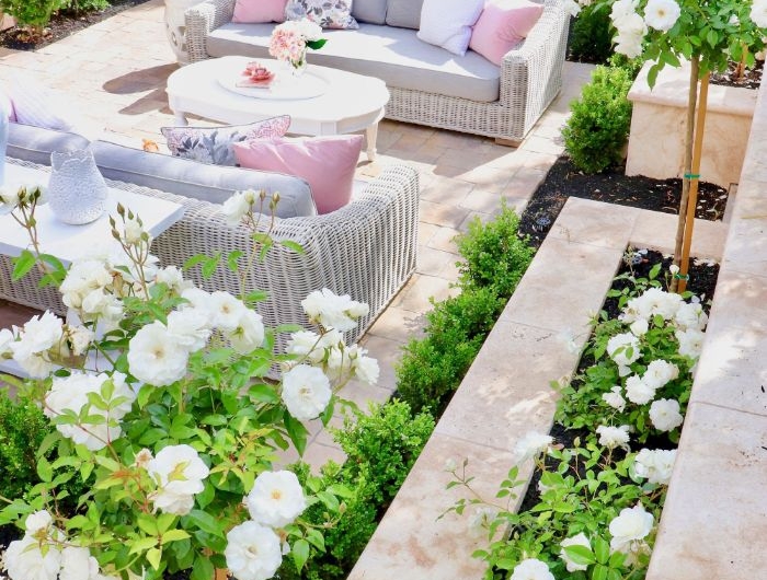 salon de jardin cocooning en résine tressée au milieu d un jardin entourée de plantes en bordure fleurs blanches