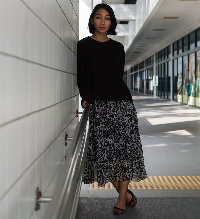 tenue classe femme avec un pull noir tricotée et une jupe midi aux imprimés
