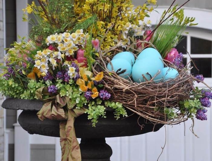 un cache pot en metal rempli des fleures printanieres et des oeufs decoratifs devant une maison