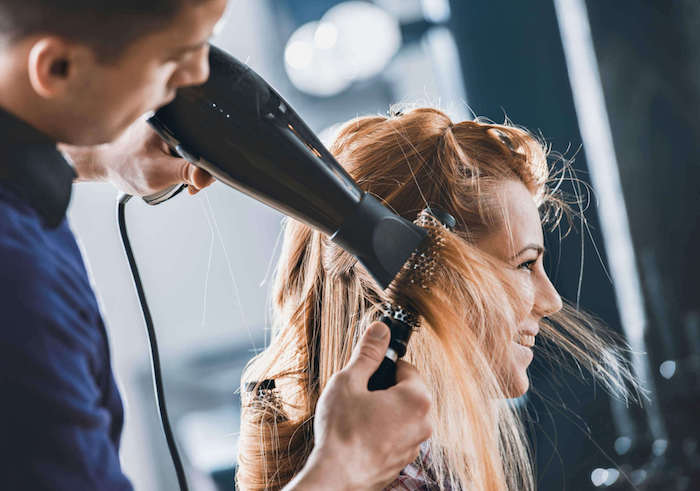 un coiffeur qui seche des cheveux abimés d une femme avec une brosse ronde et sèche cheveux