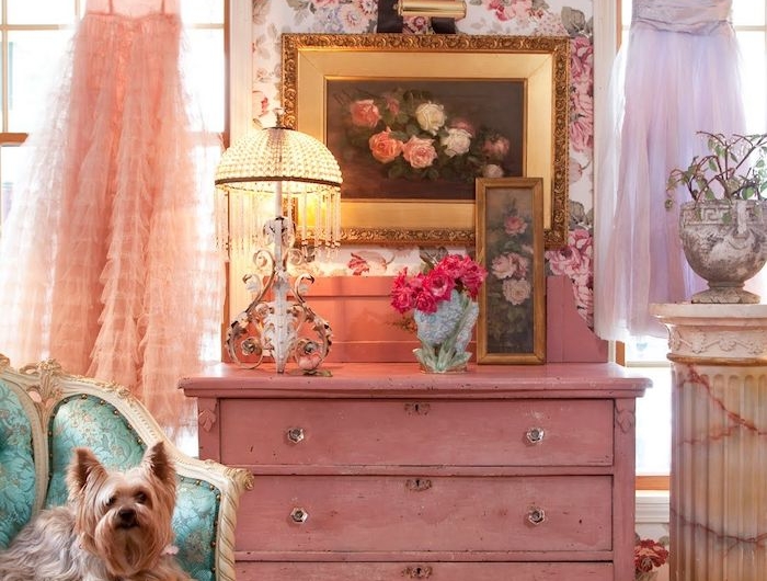 un comode rose devant un mur aux papiers peintts floraux une robe suspendu de la fenetre deco chambre rose