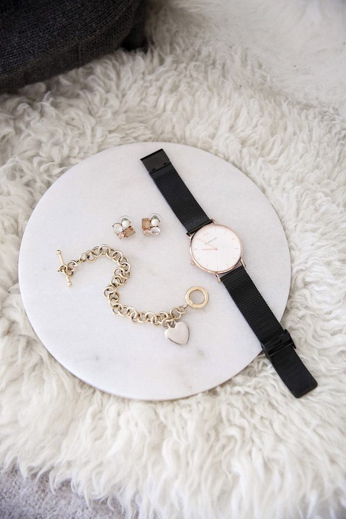 un montre et bracelet dorée sur un plateau ronde posé sur un tapis blanc accessoires style minimaliste