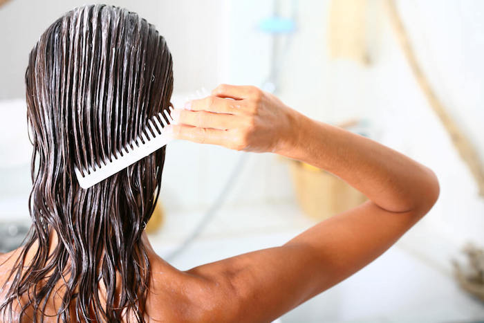 une femme dans la salle de bain qui peigne ses cheveux onctués d un masque hydratant cheveux maison