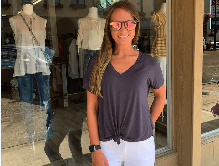 une femme devant la vitrine d une boutique avec un t shirt violet rentré dans un pantalon blanc jpg