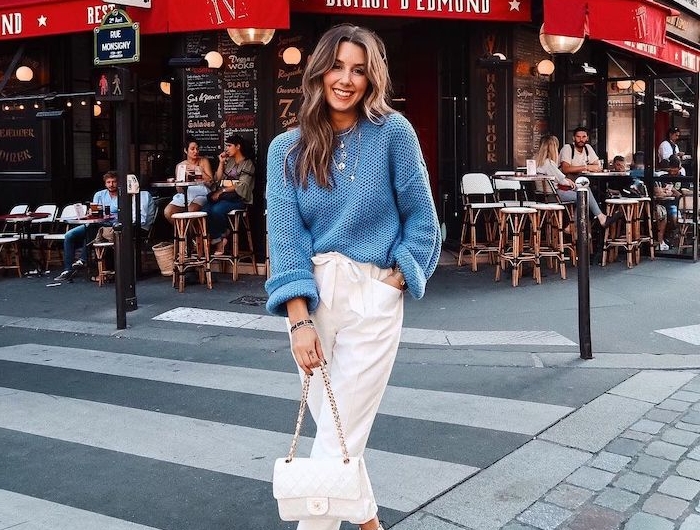 une femme devant un café vetue en pull bleu tricoté et pantalon streetwear