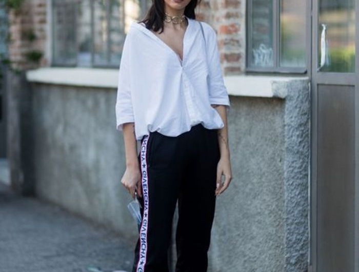 une femme qui porte pantalon streetwear et une chemisier blanc ample devant un batiment