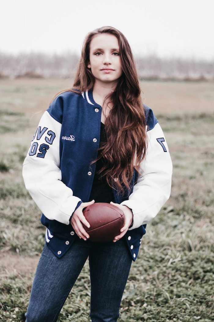 une femme vetue en jean foncé et une veste américaine qui tient une balle de rugby