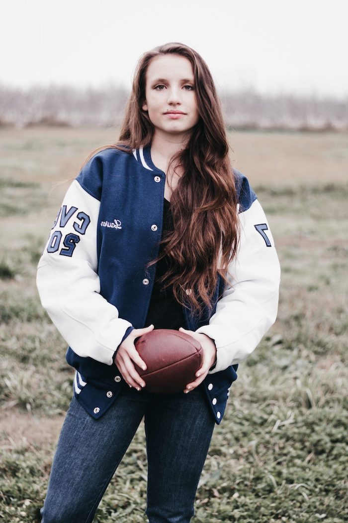 a woman dressed in dark jeans and an American jacket with a rugby ball