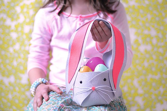 une fille qui tient une décoration de paque facile panier en forme de lapin rempli des oeufs en plastique