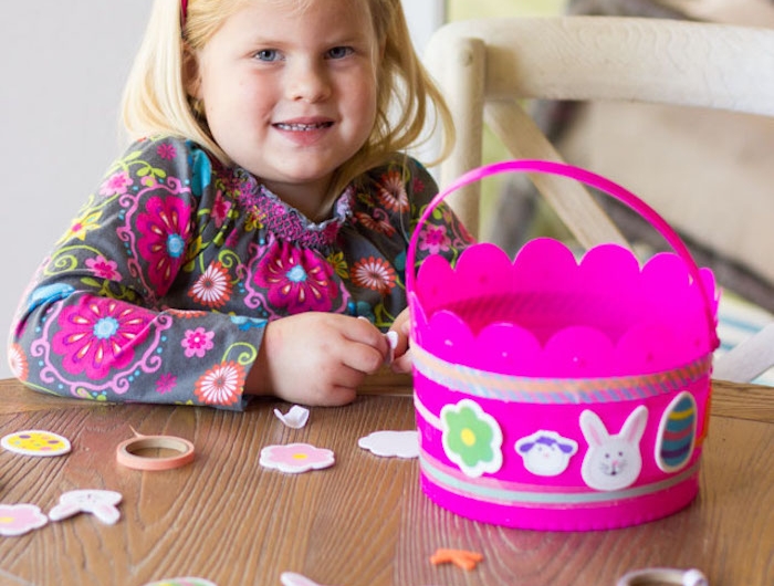 une jolie petite fille blonde qui fait un bricolage paques primaire avec un panier en plastique rose et des autocollants