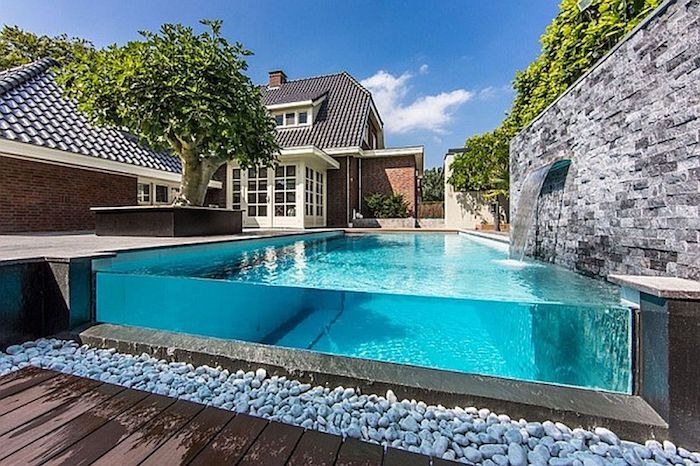 une piscine devant grande maison avec une ligne des galets devant l une de ses cotés