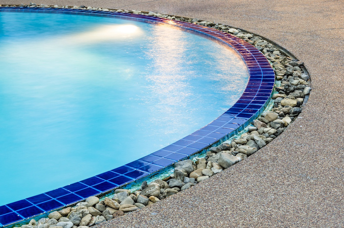 une piscine entourée d une bordure des pierres décoratives et des carreaux bleus