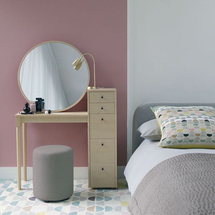 une tabourette devant une toilette en bois avec un miroir rond dans un chambre gris et rose 
