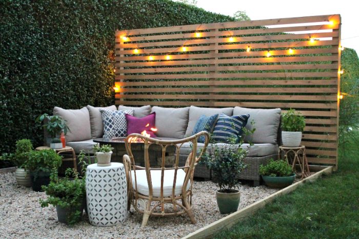 cloture en palette de bois décorée de guirlande lumineuse salon de jardin tressé sur gravier avec des plantes en pot