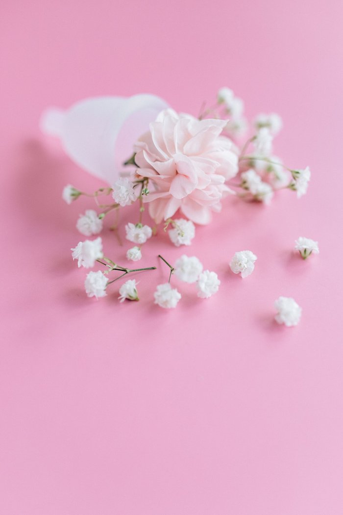 coupe menstruelle blanche une fleur rose dedans et brins de muguet persemés