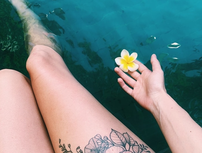 deux jambes dans la mer avec tatouage ornemental des fleurs et une fleur de hawaii