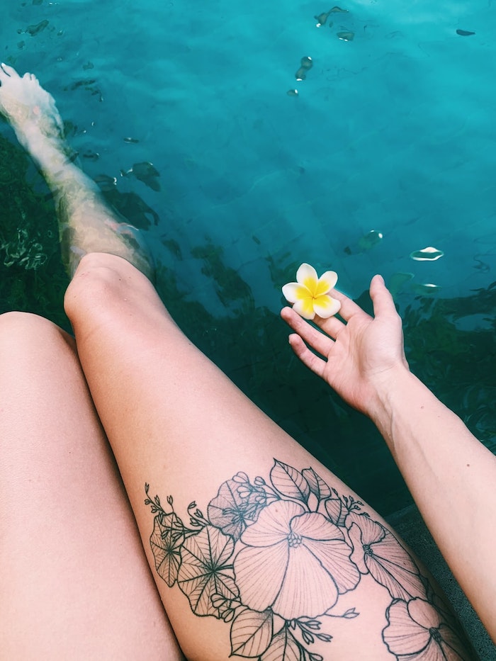 deux jambes dans la mer avec tatouage ornemental des fleurs et une fleur de hawaii