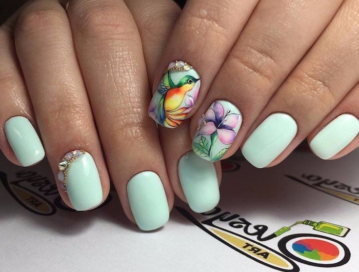 deux mains avec des ongles en couleur menthe et des dessins fleur et oiseau