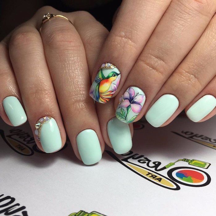 deux mains avec des ongles en couleur menthe et des dessins fleur et oiseau