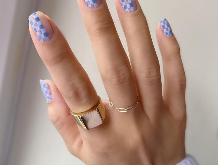 ongles pastel multicolores avec des petits formes geometriques sur un main avec bagues dores