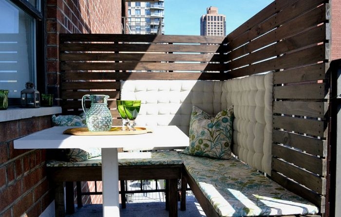 palissade en palette recyclée sur balcon aménagé avec des bancs de bois coussins et housses mur de briques
