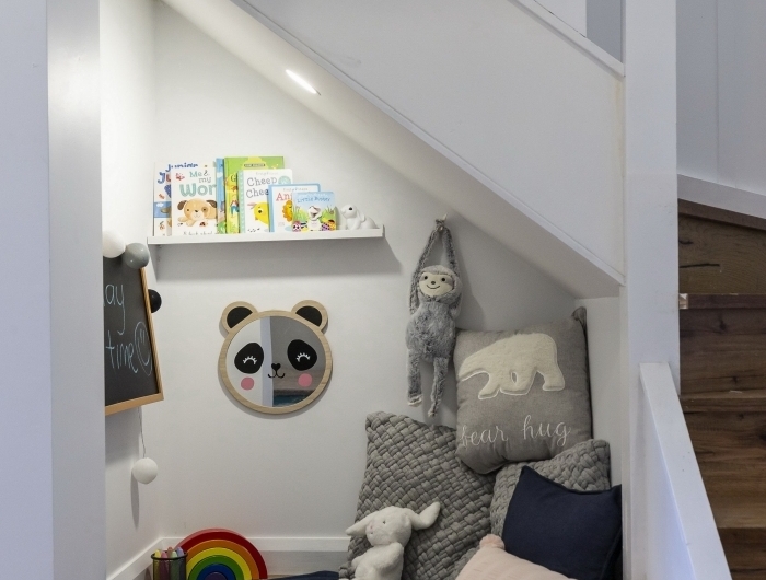 tapis rond étagère bois blanc aménagement sous escalier ouvert coussins gris jouets coin de jeux couloir