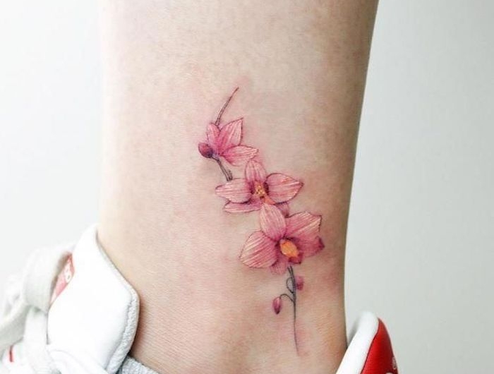 un cheville du jambe qui porte des baskets adidas blanches avec un fleur de cerisier tatouage minimaliste