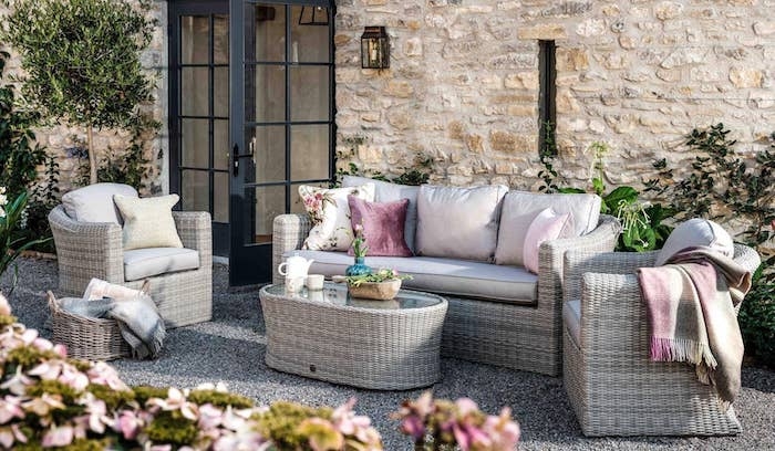 un ensemble des meubles en rotin devant une grande maison en pierre avec des coussins et des fleurs roses